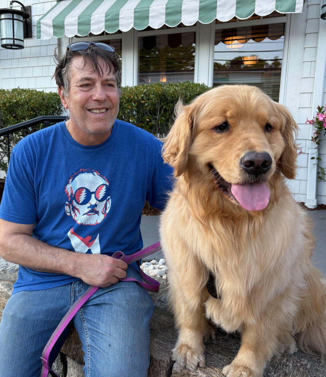Andy and Honey, a golden retriever, sitting together on a low stone wall.